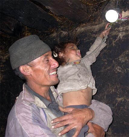 Man holding child reaching for electric light bulb in a home in Humla, Nepal.